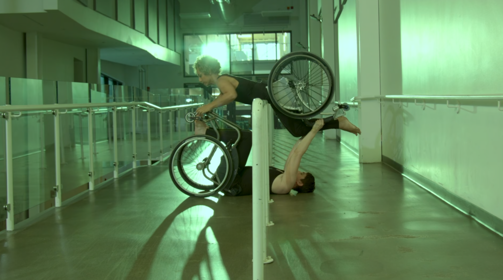 Still from dance film Inclinations by Danielle Peers and Alice Sheppard showing two dancers in a wheelchair performing on an accessible ramp