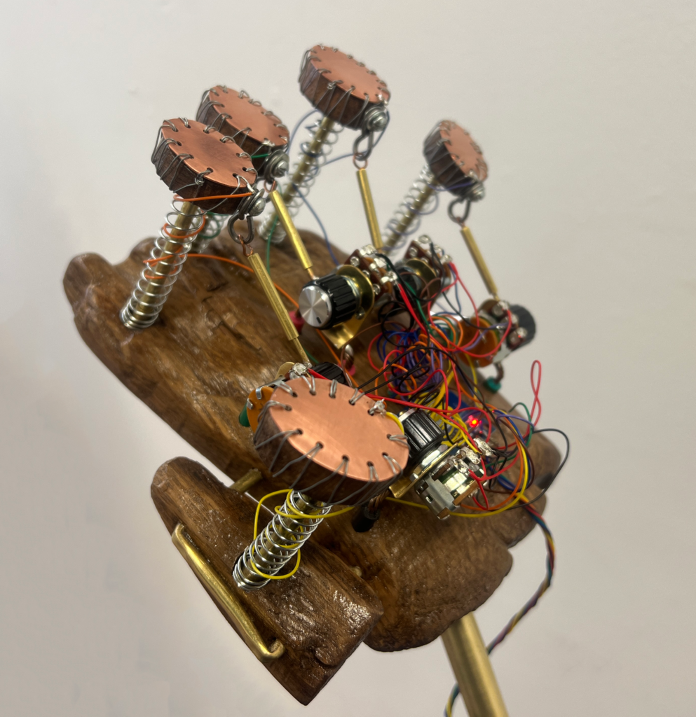 A palm shaped plank of wood, intricately woven with circuitry and springs that protrude from the tips, topped with copper and supported by brass