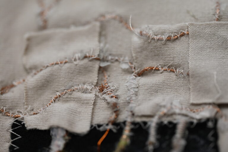 Close-up of fabric patch construction, showing copper conductive thread stitched between garment panels.